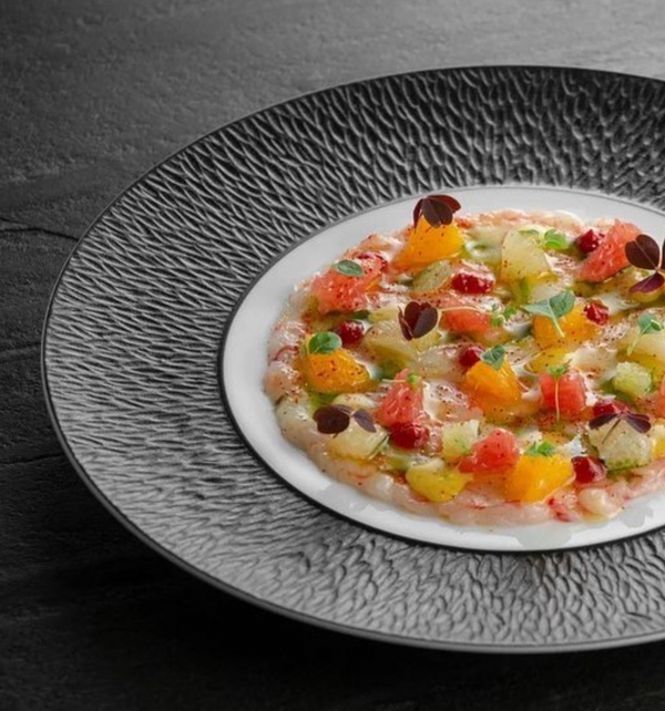 A gourmet dish is artfully presented on the Mineral Irise Dinnerware Dark Grey by Raynaud, with vibrant fruit and herb pieces atop a translucent base, garnished with microgreens for a striking, colorful display.