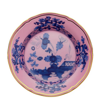 The Ginori 1735 Oriente Italiano Dinnerware Azalea is a round Italian porcelain plate with a pink background, detailed blue chinoiserie floral motif, and gold rim in a timeless traditional style.