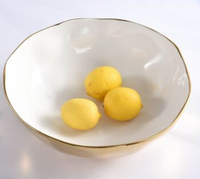 Three yellow lemons rest in a PAMPA BAY Moonlight Bowl, crafted from white porcelain with a gold titanium rim and set on a white surface.