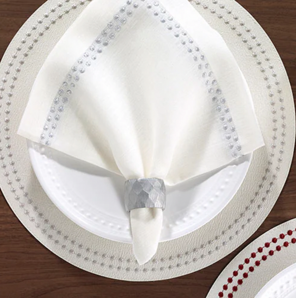 A white plate on a matching placemat features a Bodrum Pearls Napkin Silver Set of 4, finely crafted from linen and folded in a silver napkin ring, all elegantly arranged atop a wooden table.