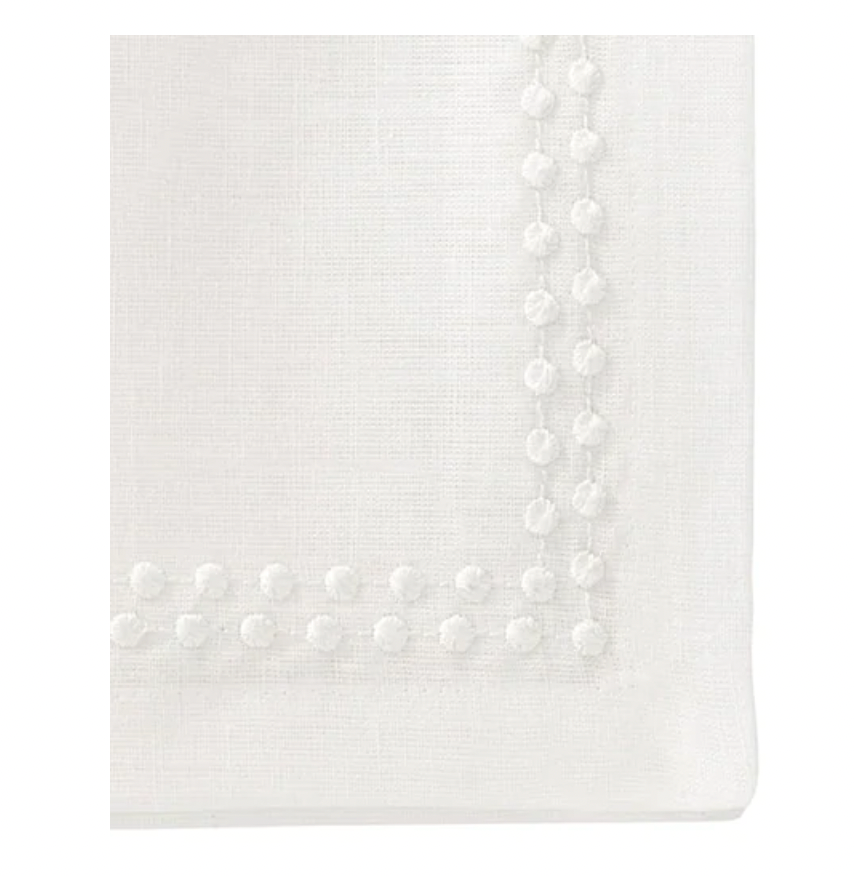 Close-up of a Bodrum Pearls Napkin White Set of 4, crafted from fine linen with a textured dotted border reminiscent of embroidered edges on a smooth, clean surface.