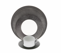 A white Limoges porcelain cup and saucer sit before a set of Haviland Anthracite Infini Dinnerware Grey plates, which feature textured radiating line patterns, all arranged on a white background.