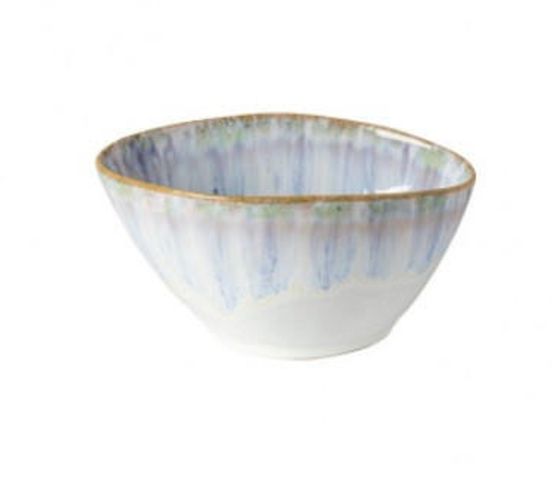 The Costa Nova Brisa Blue Dinnerware bowl features a rounded square shape, white base with blue vertical streaks, and a thin brown rim. This ceramic piece is empty and displayed against a plain white background.