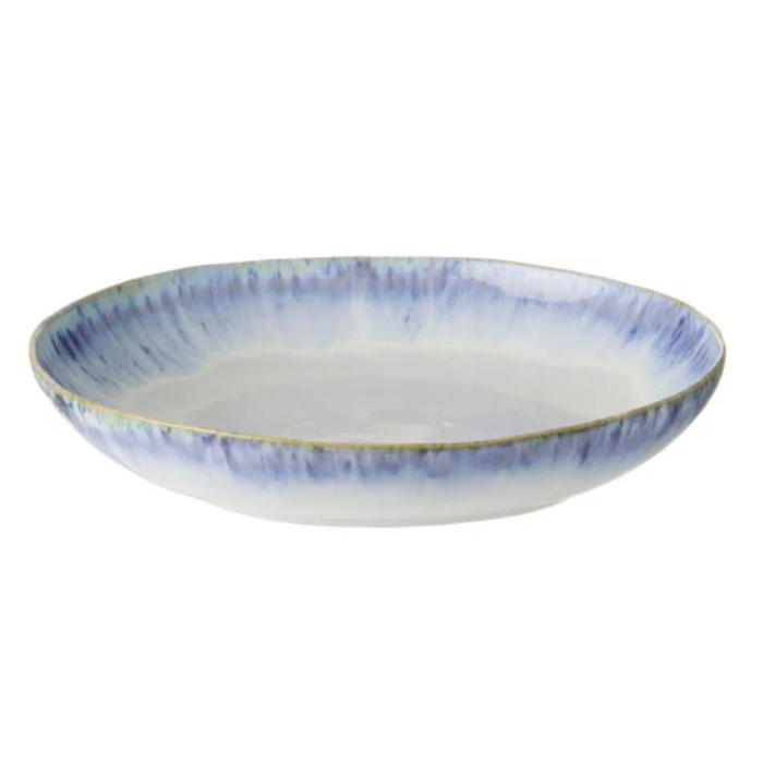 The Brisa Blue Dinnerware shallow ceramic bowl by Costa Nova features a white interior, blue watercolor-style rims, and a golden edge; each stoneware piece is thoughtfully crafted in Portugal.