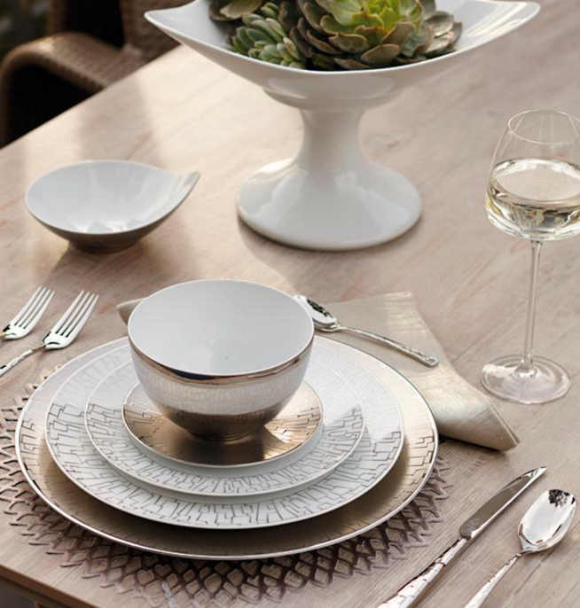 Elegant table setting with Rosenthal Skin Platinum TAC 02 dinnerware—layered white plates with platinum accents, a bowl, silver cutlery, a wine glass of white wine, beige napkin, and succulent centerpiece in a white dish on a wooden table.