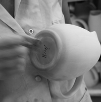A person in a buttoned shirt examines the base of a Jars Wabi Seidou Dinnerware teapot marked “France.” The black and white image highlights its smooth, artisanal ceramic texture and unique tableware charm.
