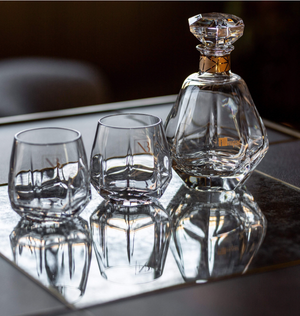 The Vista Alegre Gemstone Crystal DOF Set of 2 features exquisite tumblers, which shine elegantly on a mirrored tray and create stunning reflections beneath them.