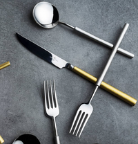 The Vista Alegre Domo Matt Gold Flatware 5 Piece Setting, featuring metallic and gold handles, is elegantly arranged on a dark gray textured surface.