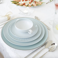 A formal table is set with Vista Alegre Trasso Dinnerware, silver cutlery, a teacup, pink drink, lemon water, and a platter of rolled vegetable appetizers atop a white tablecloth.