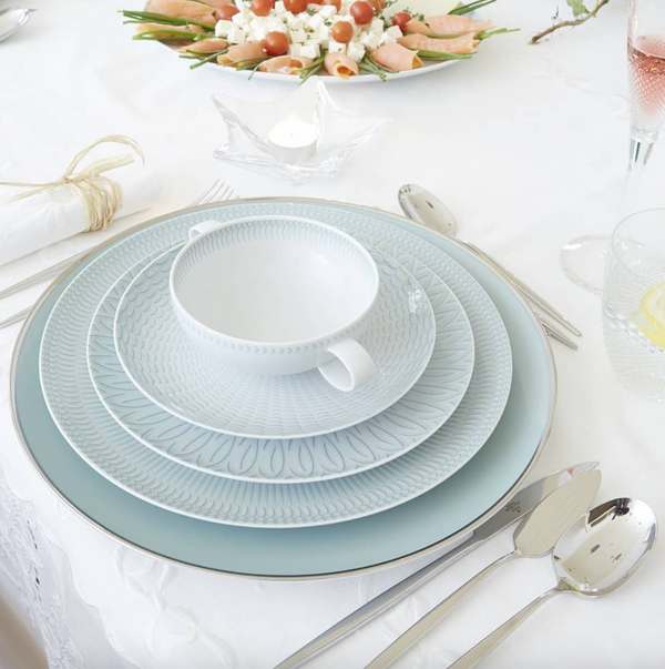 A formal table is set with Vista Alegre Trasso Dinnerware, silver cutlery, a teacup, pink drink, lemon water, and a platter of rolled vegetable appetizers atop a white tablecloth.