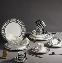 A Greg Natale Palazzo Navy Dinnerware 3 Piece Set of plates, bowls, and cups—some stacked—crafted from fine bone china sits with a gold spoon, fork, pastel macarons, and a silver spoon on a grey background.