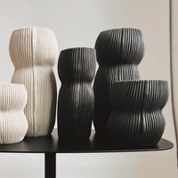 The Curvy Round Vase Black by CYM Warkov Ceramics, with its vertical grooves and organic curves, is arranged on a dark tabletop against a neutral background, highlighting the elegance of artisan pottery.