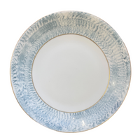 The Marie Daâge Agate Dinnerware by Marie Daâge features a round ceramic plate with a wide, textured blue and white rim, a thin gold band at the inner edge, and a plain white center—an elegant example of hand-painted porcelain.
