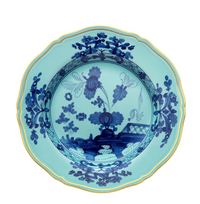 The Ginori 1735 Oriente Italiano Dinnerware Iris is a decorative blue and turquoise porcelain plate with scalloped edges, gold trim, and intricate chinoiserie floral motifs inspired by Italian design.