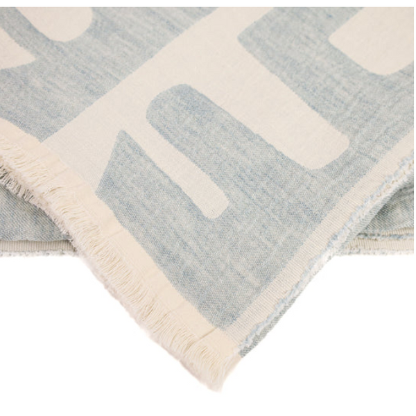 The Waters Throw Blue by Uniquity features bold, abstract botanical motifs in light blue and white woven fabric with fringed edges, crafted using traditional weaving techniques.