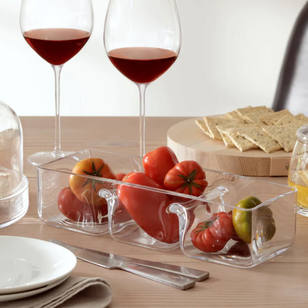A table set with two glasses of red wine, LSA's Serve Handmade Trio Dish filled with heirloom tomatoes, a plate of crackers, a jar of mustard, and a stack of white plates topped with a napkin.