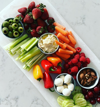 The Nashi Home Swirl Classic Resin Rectangle Platter displays green olives, strawberries, celery sticks, hummus, baby carrots, raspberries, mini bell peppers, mozzarella balls, almonds, cherries, and cucumber slices on a white surface.