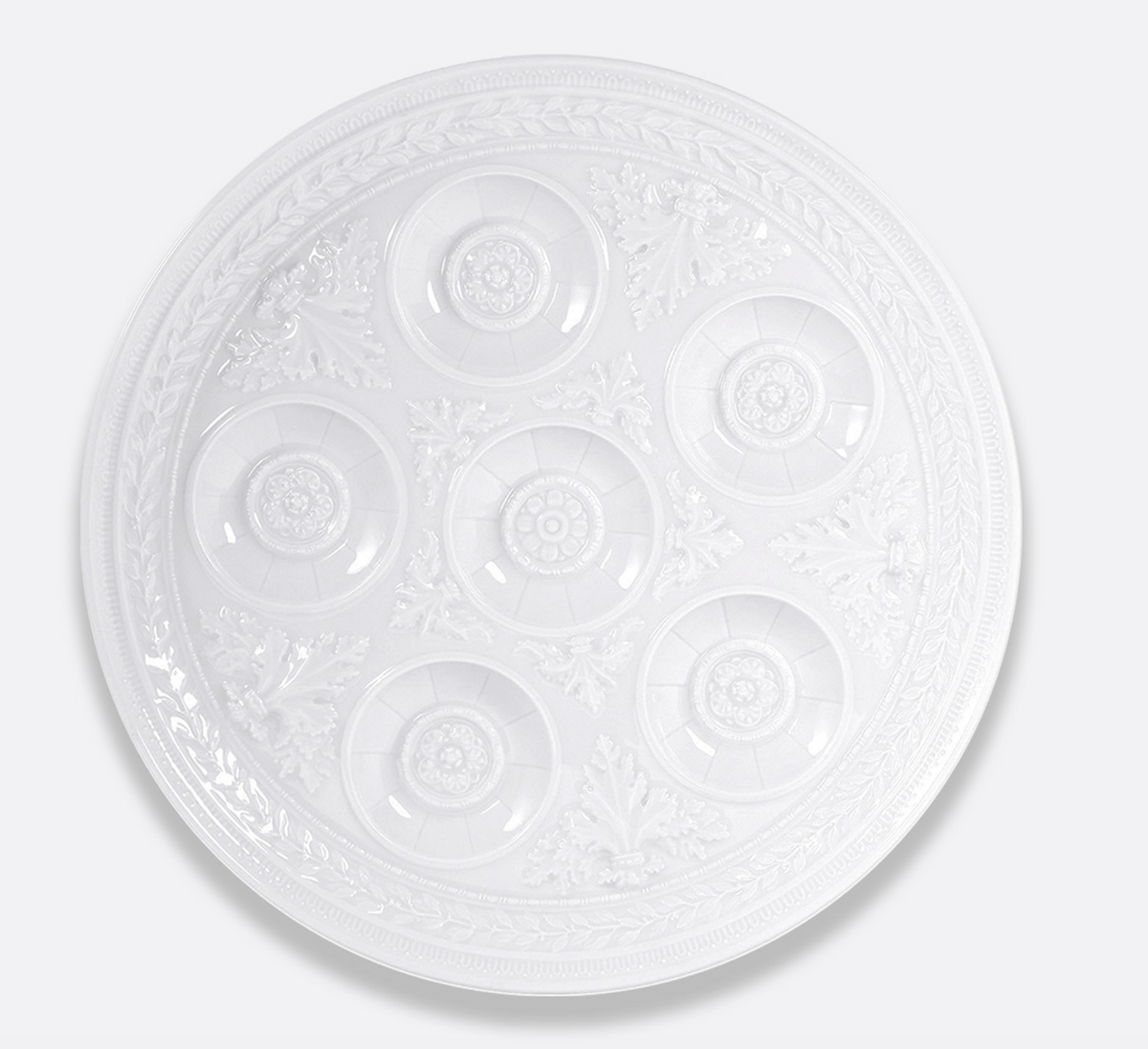 The Bernardaud Louvre Condiment Tray is a round, white, ornate plate with seven circular indentations and intricate patterns, inspired by classic Limoges France craftsmanship.