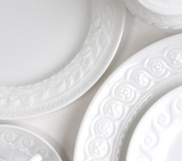 Close-up of several Bernardaud Louvre Condiment Trays, featuring ornate embossed rims inspired by French architecture, arranged overlapping on a light surface.