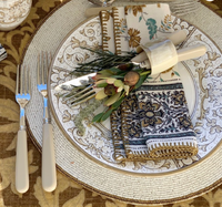 The Von Gern Home Graphic Sparkle Placemats Set of 4 creates a sophisticated table with patterned plates, ornate napkins, white-handled cutlery, cream utensils, and decor featuring greenery, acorns, and woven leaf accents.