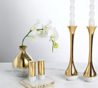 A gold and marble vase with white orchids sits next to two gold and white candlesticks and the Anna New York Dual Salt & Pepper Shakers Marble & Gold Set of 2 on a sleek Italian Carrara Marble surface.