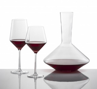 Two Tritan Crystal Glass wine glasses filled with red wine and a Zwiesel Fortessa Zweisel Pure Red Wine Decanter rest on a reflective surface against a white background.