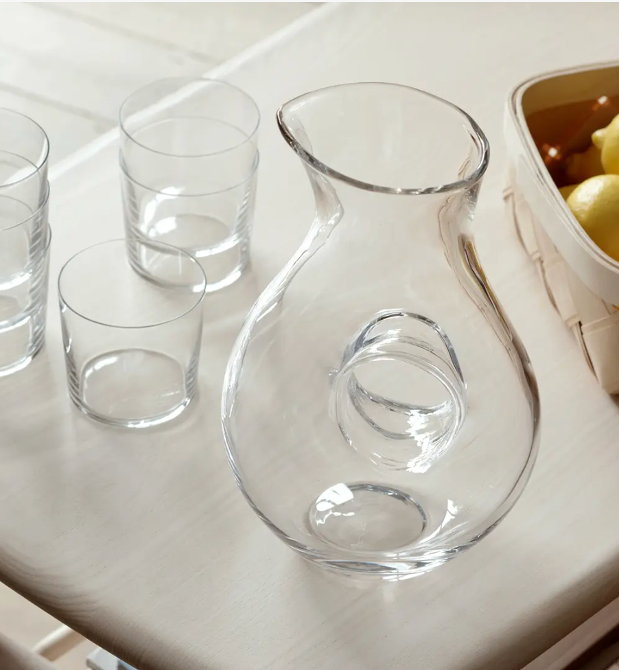 The LSA Ono Jug with its signature round handle sits on a light table beside four empty glass tumblers and a basket of yellow lemons.