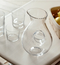 The LSA Ono Jug with its signature round handle sits on a light table beside four empty glass tumblers and a basket of yellow lemons.