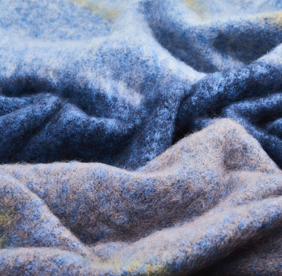 A close-up of a Boher Extra Large Throw by Cushendale, folded to highlight its fuzzy mohair texture in varying shades of blue, grey, and hints of yellow.