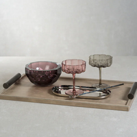 A textured glass bowl, two colored glass goblets, a small metal tray, and chopsticks are neatly arranged on the Zodax Belle Rectangle Leather Tray—its beige leather surface and dark handles creating an elegant and refined presentation.