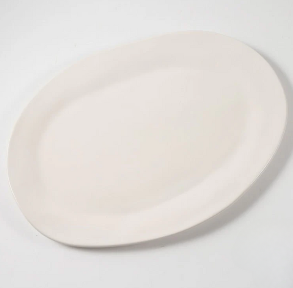 The Oval Platter Large 19" by Alex Marshall Studios, a large, oval-shaped plain white ceramic plate with artisan elegance, is displayed empty and slightly tilted on a white background.