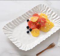 The PAMPA BAY Mascali Bianca Deep Tray displays sliced grapefruit, orange, strawberries, and blueberries, with a small wooden fork beside it on a white surface.