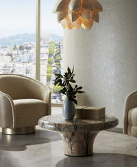 A modern living room with large windows, two curved cream armchairs, and a marble coffee table featuring the Arteriors Yancy Vases Set of 2. Decorative boxes and a sculptural pendant light complete the space with city views and greenery outside.