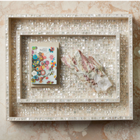 The Graceland Mother Of Pearl Tray by Currey & Company displays a vibrant floral notebook and crystals, adding an elegant luxury decor accent to your marble surface.