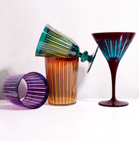 The Prism Wine Glass Set of 4 by L'Objet features colorful glasses in purple, amber, green, and blue with vertical ribbed patterns, arranged playfully on a white surface.