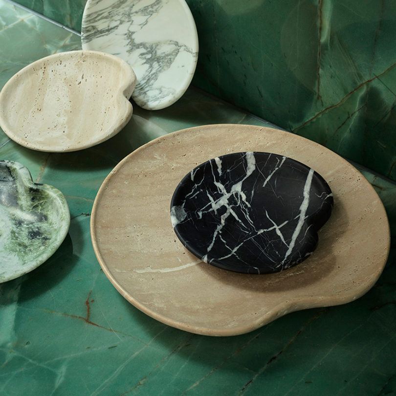Four uniquely shaped Lily Marble Bowl Black dishes by Greg Natale, each with a distinct pattern, are artfully arranged on a green marble surface, blending classic materials with modern design.