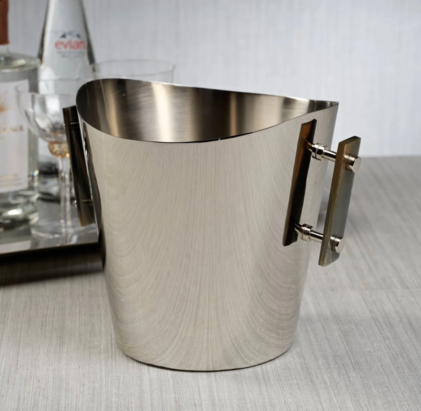 The Zodax Belmont Wine Cooler / Ice Bucket - Small, featuring two rectangular side handles, sits on a light surface with a tray of bottles and glasses subtly blurred in the background.