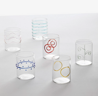Six clear water glasses from the Deco Arlecchino Water Glass Set of 6 by Ichendorf Milano are shown on a plain white background, each featuring unique mixed color patterns like squiggles, circles, dots, and wavy lines.