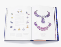 An open book, "Sapphire: A Celebration of Color" by W.W. Norton Company, displays vivid jewelry illustrations—smaller designs on the left page and striking purple gemstone necklaces and collars on the right, evoking a luxurious style.