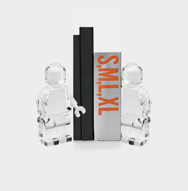 Two transparent Luho Brix Sculpture Lego-style figurines stand beside three upright books, one with "SMXL" in bold orange on the spine—adding a playful touch to any home decor against a white background.