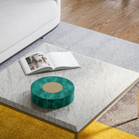A marble coffee table topped with an open book and the Archer Green Round Box by Currey & Company sits on a rug, with a sofa and wooden floor in the background.