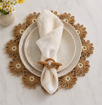 A Merritt Reactive Glaze Melamine Dinnerware Beige plate is set on a gold floral placemat with a smaller plate, a cream napkin with gold accents in a woven ring, all arranged on light marble. Daisies peek in from the corner.