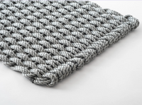 A close-up of the Coastal Woven Outdoor Floormat by The Rope Co in Weathered Gray (24 x 38), featuring thick, handwoven rope with wide, loose weaves and neatly finished edges, displayed on a white surface.
