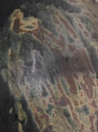 A close-up of the Devenir 1 Vase by CDMX / MASA TALLER reveals a weathered, rusted metal surface with patches of green, brown, and black—bearing the marks of corrosion and oxidation that evoke artisanal sculptural techniques.