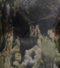 A close-up of the Devenir 2 Vase by CDMX / MASA TALLER reveals its rough, textured surface, featuring a striking blend of dark green, black, and brown patches—reminiscent of abstract camouflage or weathered metal—that highlights the unique artisanal finish of this sculptural piece.