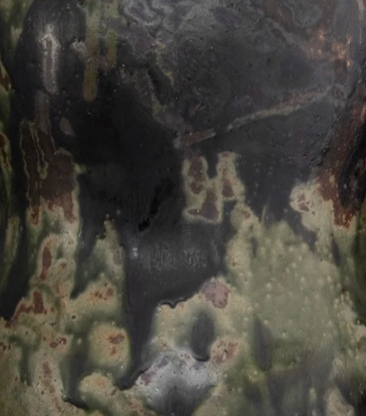 A close-up of the Devenir 2 Vase by CDMX / MASA TALLER reveals its rough, textured surface, featuring a striking blend of dark green, black, and brown patches—reminiscent of abstract camouflage or weathered metal—that highlights the unique artisanal finish of this sculptural piece.