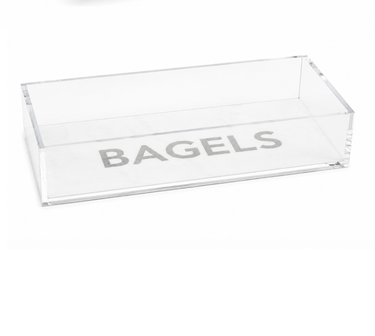 Introducing the Eye Candy Bagel Tray: a clear, rectangular acrylic container featuring the word “BAGELS” in bold gray letters on the bottom. This food-safe tray from Eye Candy makes an ideal gift for any bagel lover.