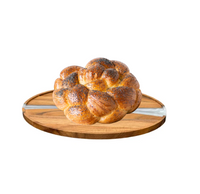 A round braided challah bread topped with poppy seeds sits on the BT-Shalom Resin and Wood Challah Board, ready to be served at the Shabbos table, set against a white background.