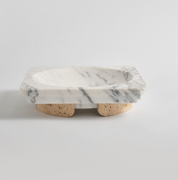 The Caldera Marble Bowl by Greg Natale features a rectangular design crafted from white marble with striking gray veining, elevated on three cork feet. Displayed against a plain white background, this elegant bowl effortlessly combines functionality with decorative appeal, bringing understated sophistication to any space.