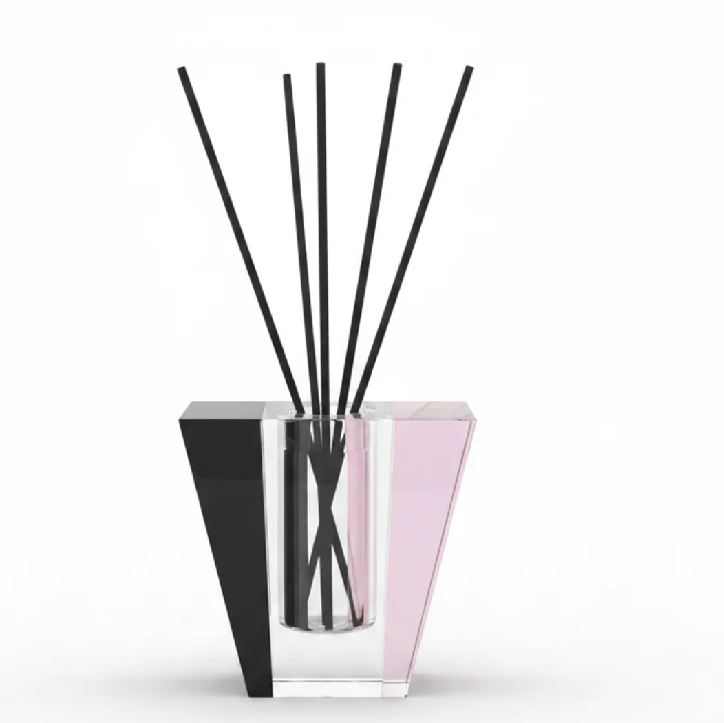 The Solar Prism Crystal Diffuser - Onyx & Rose - Elder Flower by Frave Home features a modern geometric crystal vessel with clear, pink, and black accents. Several thin black reeds stand upright against a white background, creating an elegant design perfect for infusing your space with the enchanting aroma of Elder Flower.